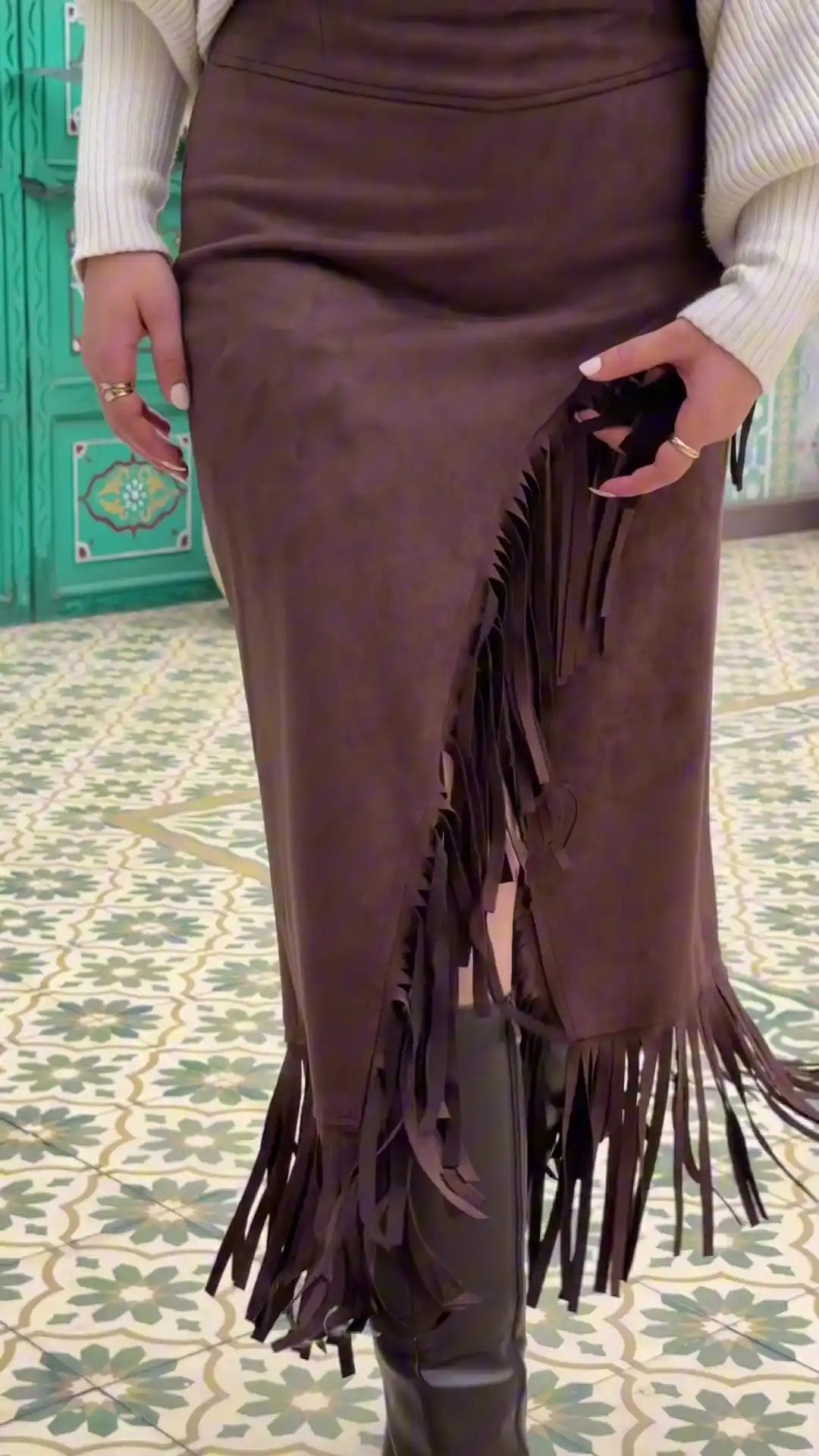Brown fringed skirt worn by a person on a patterned floor.